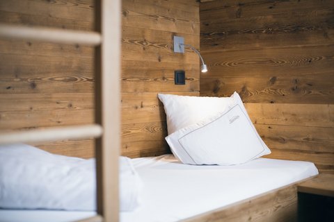 Bilder aus der Sportalm Einzelbett mit weißen Kissen und Holzwand im Hintergrund