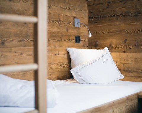 Bilder aus der Sportalm Einzelbett mit weißen Kissen und Holzwand im Hintergrund