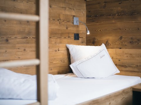 Bilder aus der Sportalm Einzelbett mit weißen Kissen und Holzwand im Hintergrund