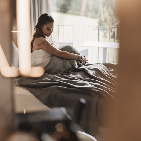 Pictures from Sportalm Woman sitting in bed with gray blanket, window view of forest