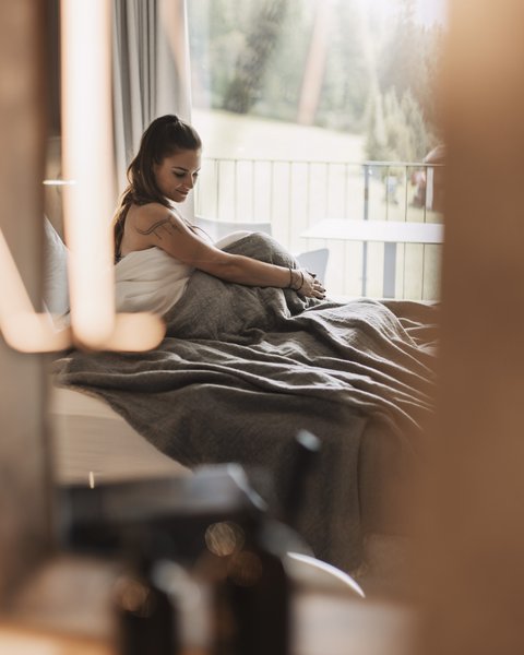 Pictures from Sportalm Woman sitting in bed with gray blanket, window view of forest