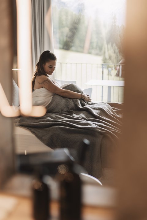 Pictures from Sportalm Woman sitting in bed with gray blanket, window view of forest