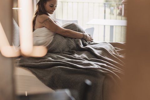 Pictures from Sportalm Woman sitting in bed with gray blanket, window view of forest