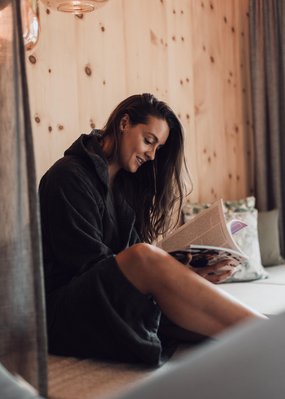 Urlaub im Pitztal? Unterkunft mit Pep! Frau in Bademantel liest entspannt ein Magazin auf einem Sofa
