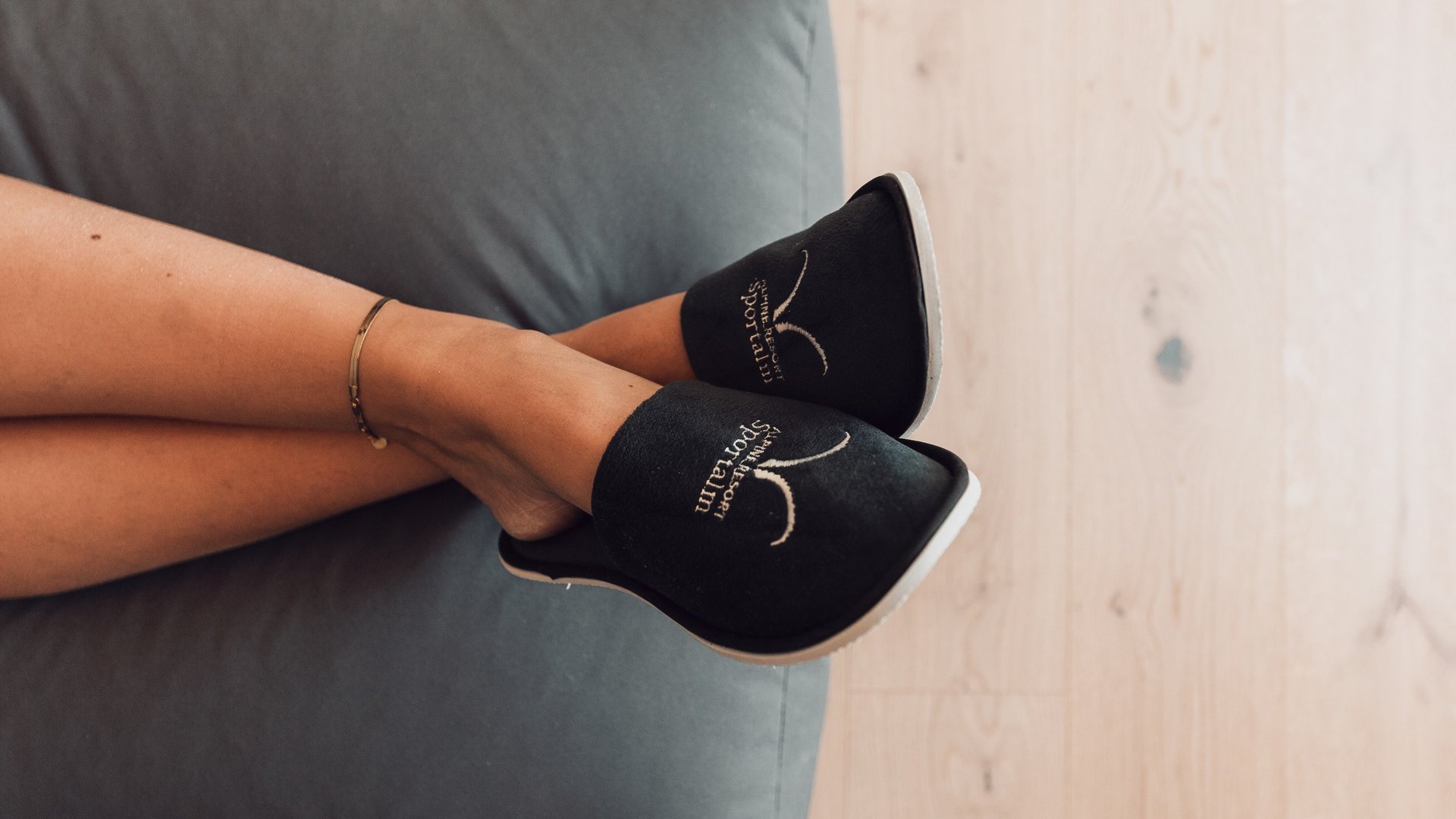 Comforting wellness treatments Person lying on sofa wearing black slippers with white logo