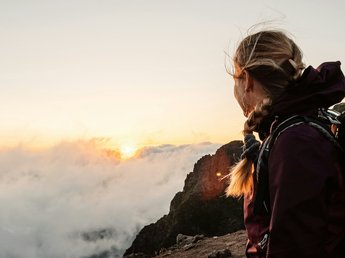 „Nuigkeiten“ aus der Sportalm Wanderin blickt bei Sonnenuntergang von einem Berggipfel auf Wolkenmeer