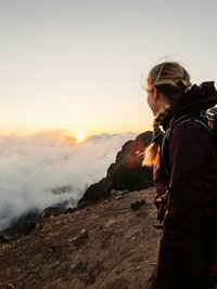Wanderin blickt bei Sonnenuntergang von einem Berggipfel auf Wolkenmeer