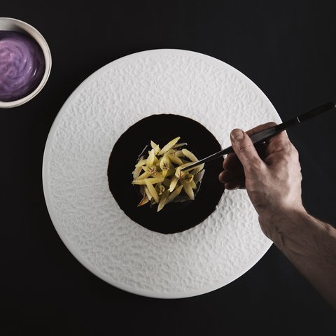 Pictures from Sportalm Hand plating fine dish with tweezers on white plate next to bowl with purple sauce
