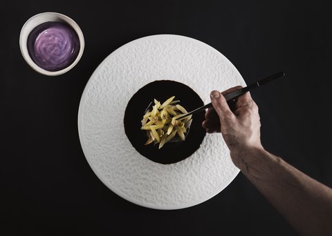 Pictures from Sportalm Hand plating fine dish with tweezers on white plate next to bowl with purple sauce