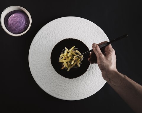 Bilder aus der Sportalm Hand richtet feines Gericht mit Pinzette auf weißem Teller an neben Schüssel mit lila Sauce