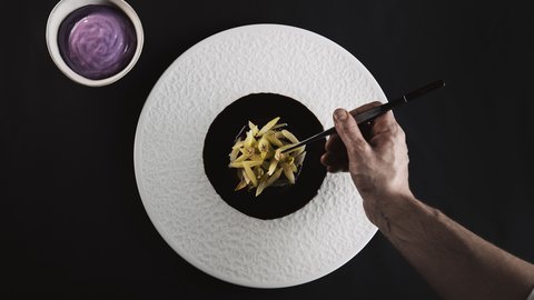 Bilder aus der Sportalm Hand richtet feines Gericht mit Pinzette auf weißem Teller an neben Schüssel mit lila Sauce