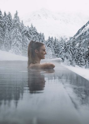 Nicht irgendein Pitztal-Resort: Alpine Resort Sportalm! Frau entspannt in beheiztem Pool umgeben von verschneiten Bergen und Bäumen