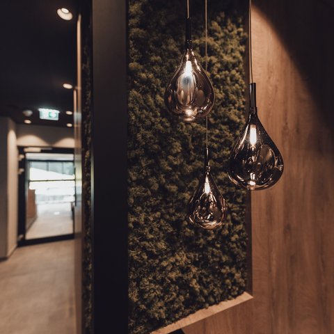 Bilder aus der Sportalm Moderne, tropfenförmige Hängelampen vor moosbedeckter Wand im Flur