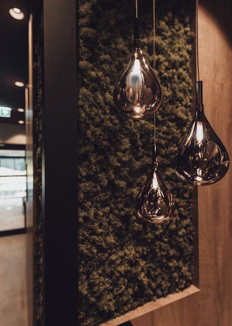 Bilder aus der Sportalm Moderne, tropfenförmige Hängelampen vor moosbedeckter Wand im Flur