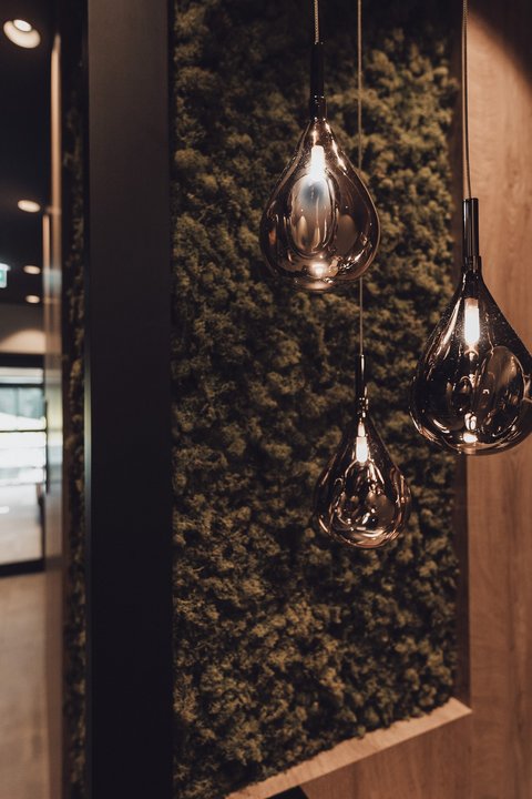 Bilder aus der Sportalm Moderne, tropfenförmige Hängelampen vor moosbedeckter Wand im Flur