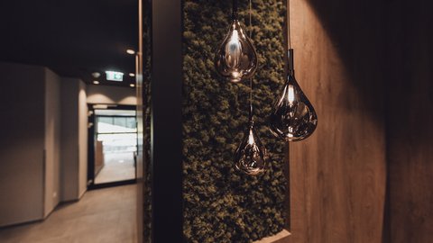 Bilder aus der Sportalm Moderne, tropfenförmige Hängelampen vor moosbedeckter Wand im Flur