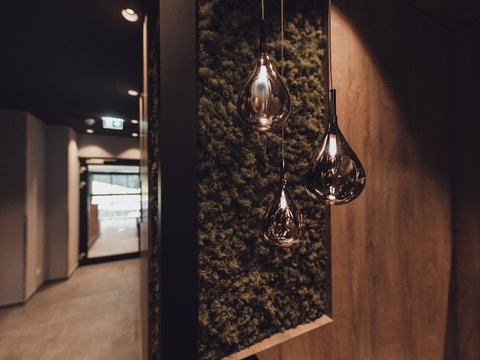 Bilder aus der Sportalm Moderne, tropfenförmige Hängelampen vor moosbedeckter Wand im Flur