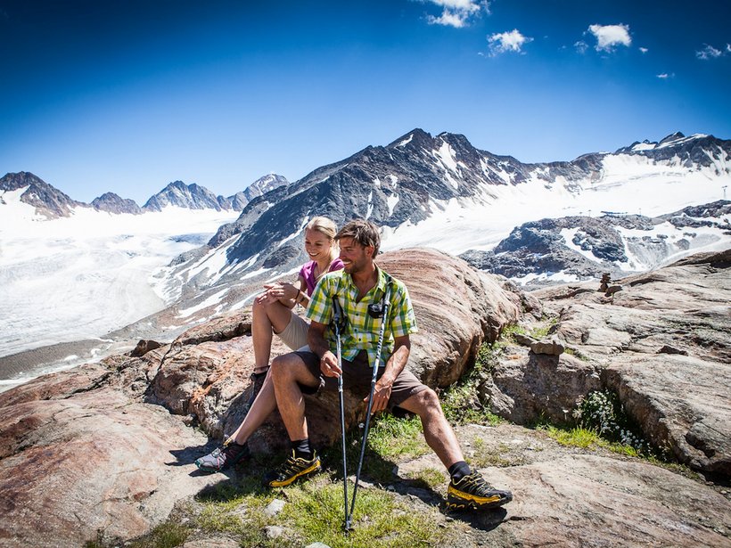 Active holidays at our sports hotel in Pitztal Couple resting on rocks while hiking with glacier and mountains in the background