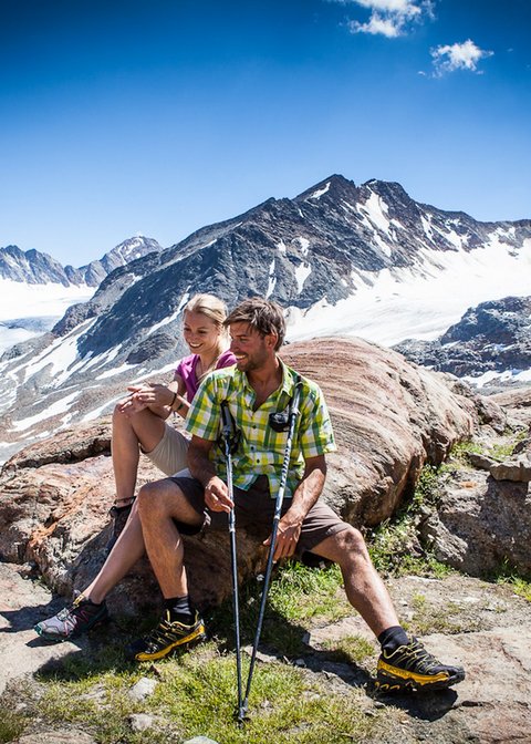 Nicht irgendein Pitztal-Resort: Alpine Resort Sportalm! Paar beim Wandern macht Pause auf Felsen mit Berggletscher im Hintergrund