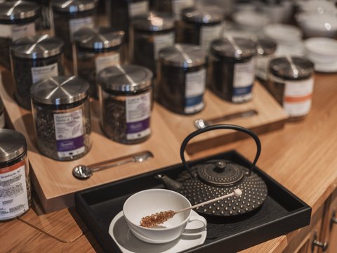 Unser Restaurant im Pitztal Teekanne, Tasse mit Rührstab und diverse Teedosen auf dem Holzregal
