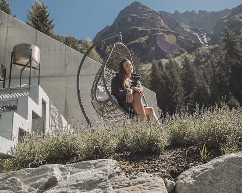 Bilder aus der Sportalm Frau entspannt in Hängesessel vor Berg und Haus bei sonnigem Wetter