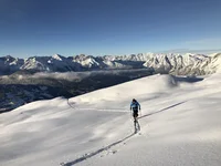 Skier ascending through fresh snow with mountains in the background