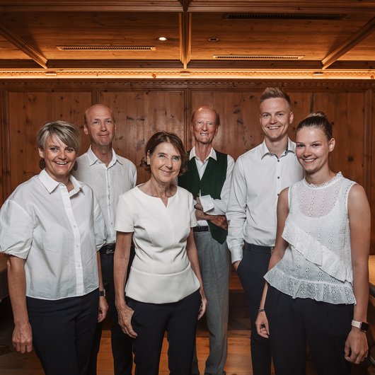 Live from St. Leonhard im Pitztal Six smiling people standing in front of a wooden wall in a rustic room