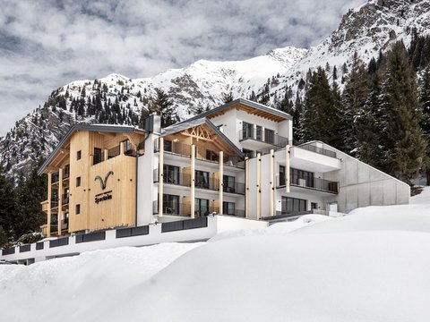 Bilder aus der Sportalm Modernes Hotel in verschneiter Berglandschaft mit Tannen und bewölktem Himmel