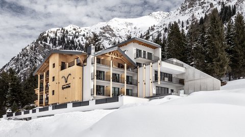 Bilder aus der Sportalm Modernes Hotel in verschneiter Berglandschaft mit Tannen und bewölktem Himmel