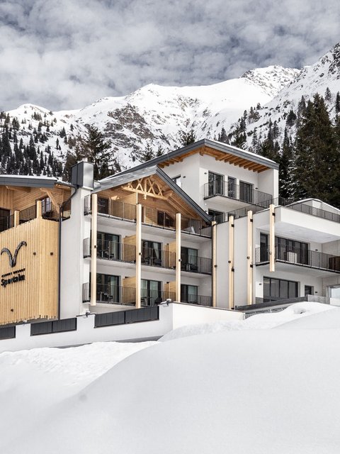 Bilder aus der Sportalm Modernes Hotel in verschneiter Berglandschaft mit Tannen und bewölktem Himmel