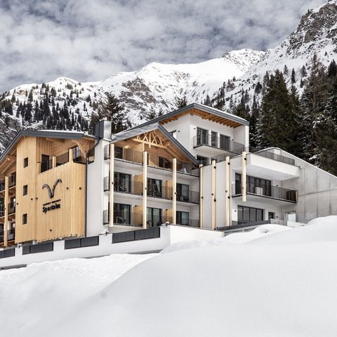 Bilder aus der Sportalm Modernes Hotel in verschneiter Berglandschaft mit Tannen und bewölktem Himmel