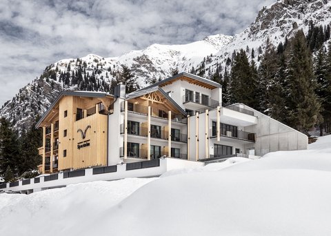 Bilder aus der Sportalm Modernes Hotel in verschneiter Berglandschaft mit Tannen und bewölktem Himmel
