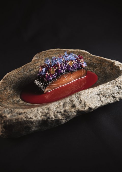 Bilder aus der Sportalm Fein angerichtetes Lachsgericht auf Felsenplatte mit roter Sauce und essbaren Blüten