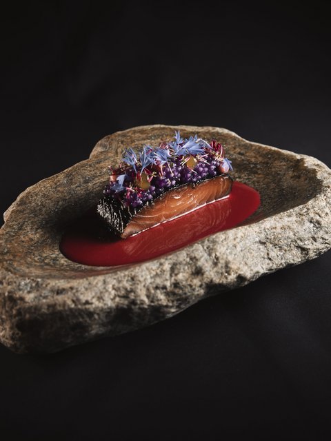 Bilder aus der Sportalm Fein angerichtetes Lachsgericht auf Felsenplatte mit roter Sauce und essbaren Blüten
