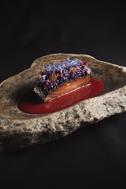 Bilder aus der Sportalm Fein angerichtetes Lachsgericht auf Felsenplatte mit roter Sauce und essbaren Blüten