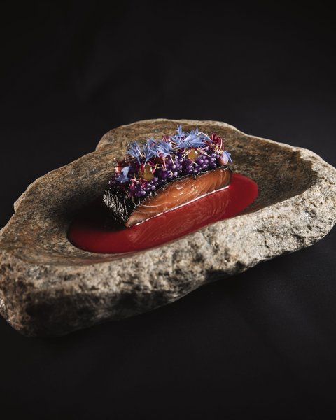 Bilder aus der Sportalm Fein angerichtetes Lachsgericht auf Felsenplatte mit roter Sauce und essbaren Blüten