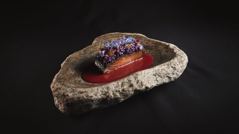 Bilder aus der Sportalm Fein angerichtetes Lachsgericht auf Felsenplatte mit roter Sauce und essbaren Blüten