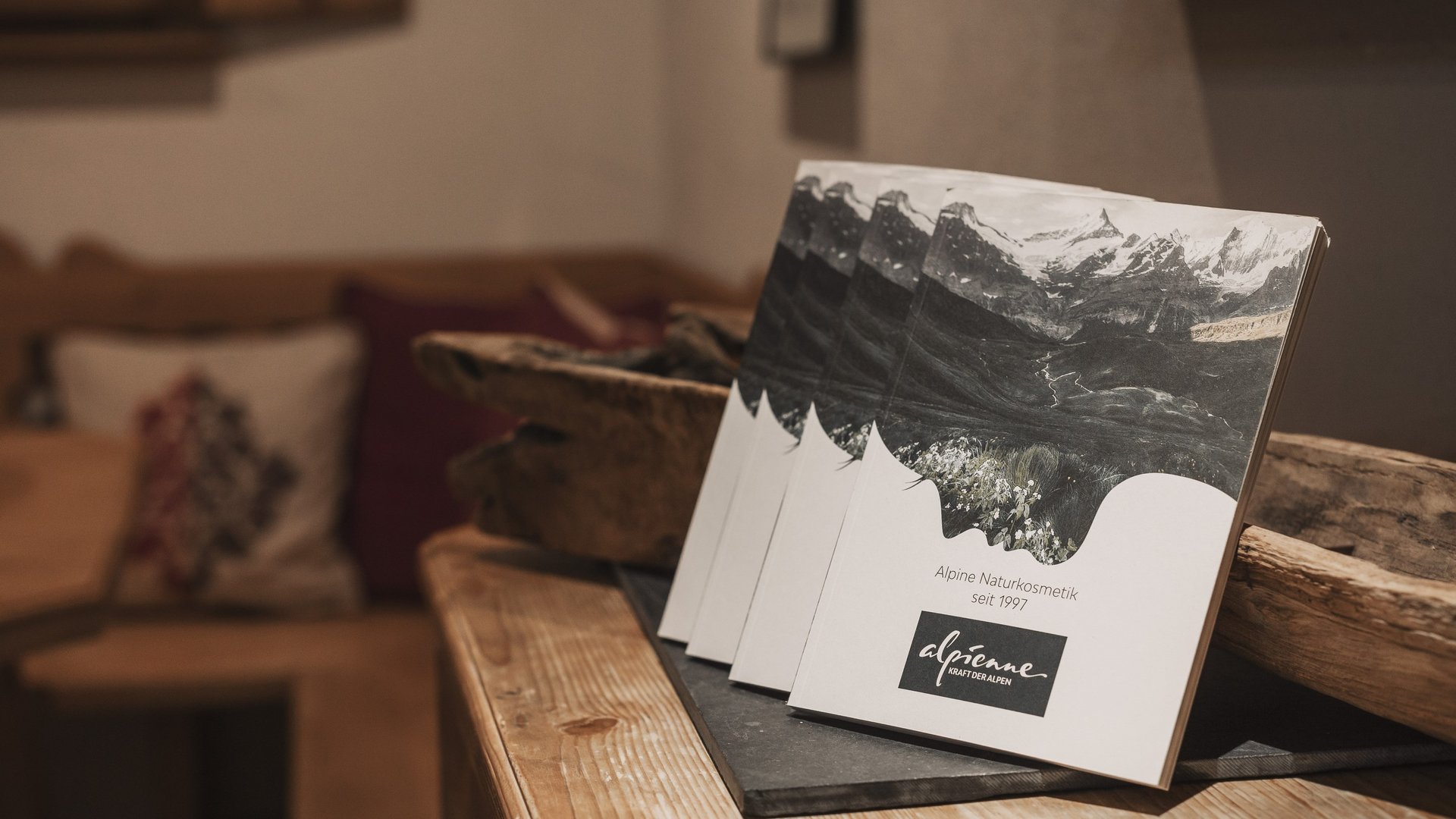 Wohltuende Wellnessbehandlungen Broschüren mit Alpenmotiv und Text zu Alpienne Naturkosmetik auf Holztisch