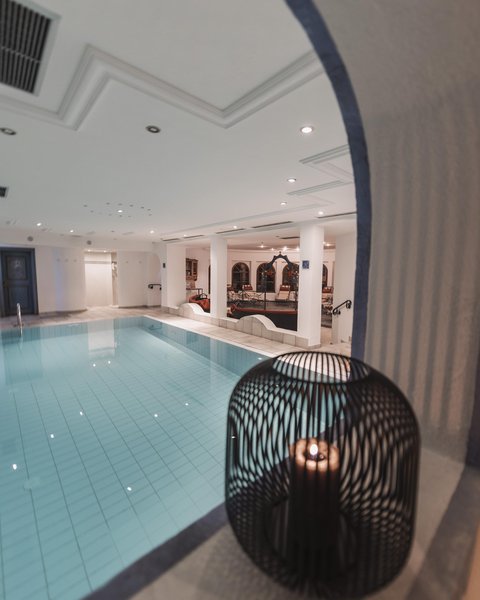 Bilder aus der Sportalm Innenbereich mit einem beleuchteten Swimmingpool und einer Kerze in einem dekorativen Käfig