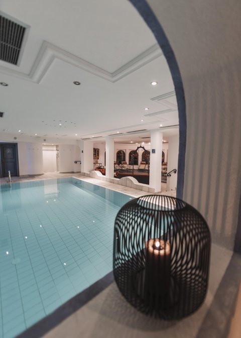 Bilder aus der Sportalm Innenbereich mit einem beleuchteten Swimmingpool und einer Kerze in einem dekorativen Käfig