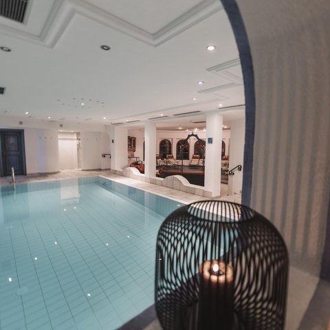 Bilder aus der Sportalm Innenbereich mit einem beleuchteten Swimmingpool und einer Kerze in einem dekorativen Käfig