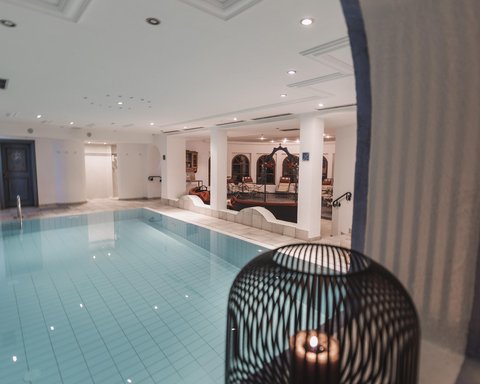 Bilder aus der Sportalm Innenbereich mit einem beleuchteten Swimmingpool und einer Kerze in einem dekorativen Käfig