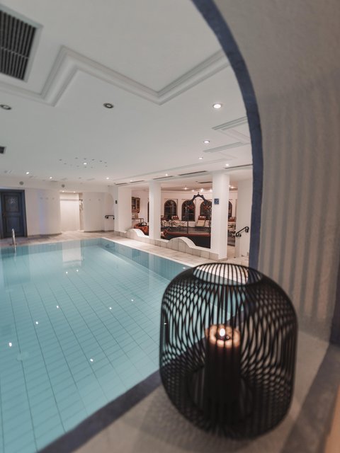 Bilder aus der Sportalm Innenbereich mit einem beleuchteten Swimmingpool und einer Kerze in einem dekorativen Käfig