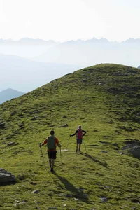 Zwei Wanderer mit Trekkingstöcken auf grünem Hügel bei Nebel in den Bergen