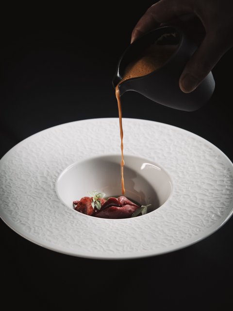 Bilder aus der Sportalm Sauce wird über eine Gourmet-Garnitur in einem dekorativen weißen Teller gegossen