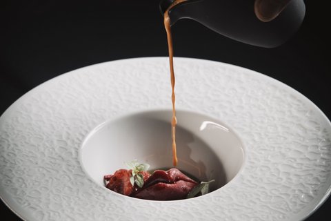 Bilder aus der Sportalm Sauce wird über eine Gourmet-Garnitur in einem dekorativen weißen Teller gegossen