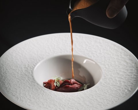 Bilder aus der Sportalm Sauce wird über eine Gourmet-Garnitur in einem dekorativen weißen Teller gegossen