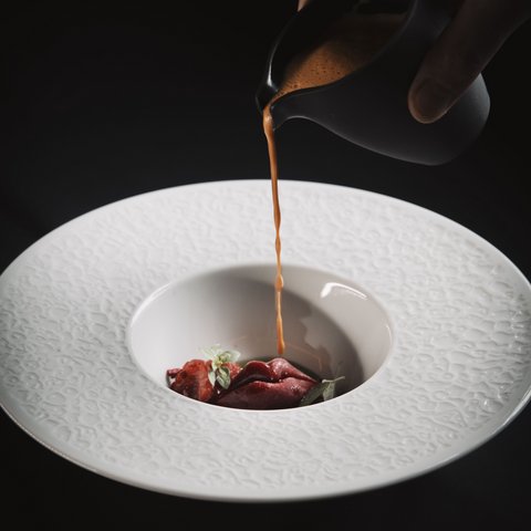 Bilder aus der Sportalm Sauce wird über eine Gourmet-Garnitur in einem dekorativen weißen Teller gegossen