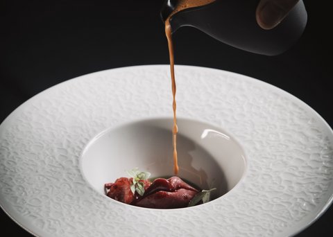 Bilder aus der Sportalm Sauce wird über eine Gourmet-Garnitur in einem dekorativen weißen Teller gegossen