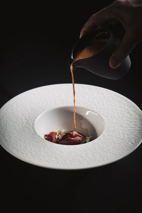 Bilder aus der Sportalm Sauce wird über eine Gourmet-Garnitur in einem dekorativen weißen Teller gegossen